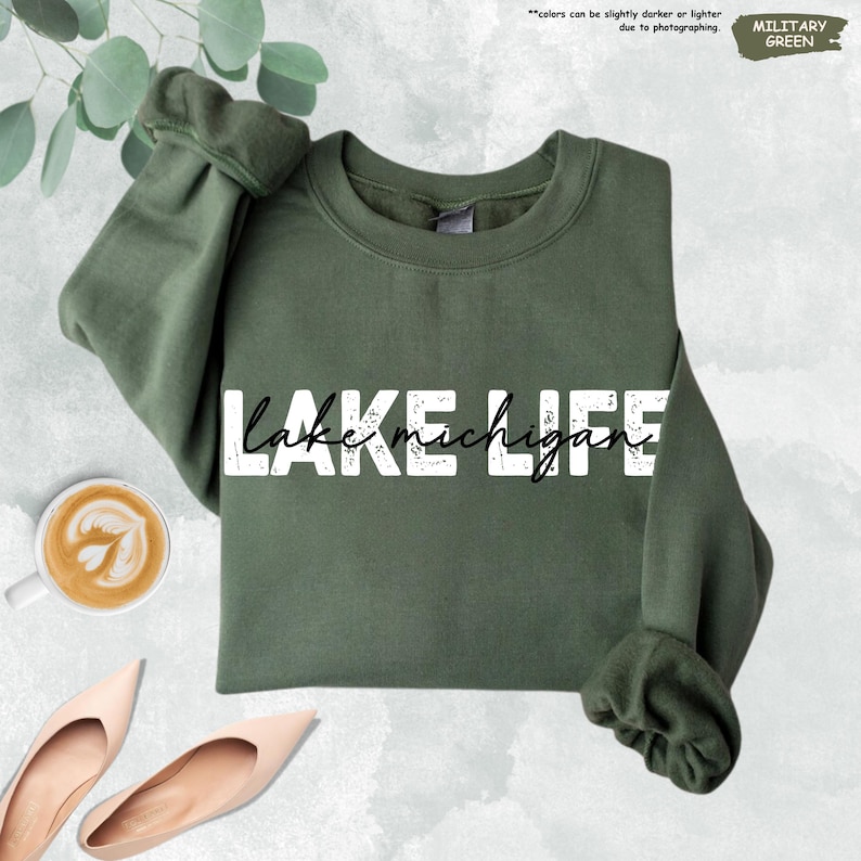 Peut inclure: Un sweat-shirt &agrave; col rond vert militaire arborant le texte blanc vieilli "LAKE LIFE" avec le texte cursif noir "lake michigan" superpos&eacute;. Le v&ecirc;tement pr&eacute;sente des manches longues avec des poignets et un col c&ocirc;tel&eacute;s.