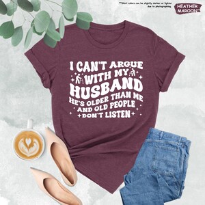 May include: Heather maroon t-shirt with white text that reads "I can't argue with my husband he's older than me and old people don't listen". The text is in a retro font style with stars and a walking stick graphic.