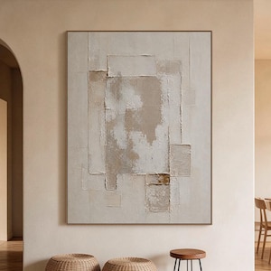 May include: A large rectangular wall art piece featuring a textured, layered composition in shades of beige, cream, and off-white. The artwork displays geometric shapes with visible impasto paint strokes, creating a tactile surface.