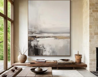 May include: Abstract landscape painting in a large, rectangular format. The artwork features a neutral color palette of white, gray, black, and gold. The brushstrokes create a textured effect, evoking a sense of depth and atmosphere. The painting is framed in a simple, light brown wooden frame.