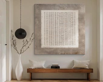 Op de afbeelding: Een moderne interieurscène met een groot abstract kunstwerk in neutrale tinten. Daaronder staat een houten bank met twee crèmekleurige kussens. Een witte vaas met takken en een zwarte bolvormige hanglamp maken de minimalistische inrichting compleet.
