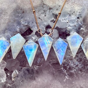 May include: Six iridescent rainbow moonstone pendants on gold chains. The moonstone pendants are faceted and have a teardrop shape.