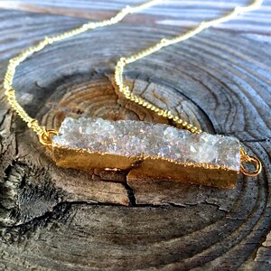 May include: A gold chain necklace with a white crystal bar pendant. The crystal bar is encased in gold metal and has a rough, natural texture.