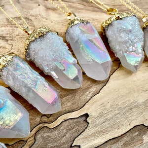 Può includere: Una collezione di sette ciondoli in cristallo di quarzo bianco iridescente con dettagli dorati su una superficie in legno. Ogni ciondolo è attaccato a una catena dorata.