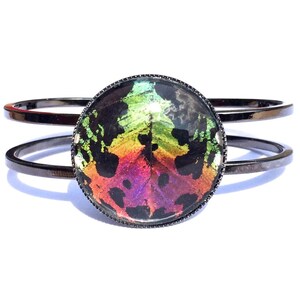 May include: A black metal bangle bracelet with a round, iridescent, multi-colored butterfly wing design in the center.
