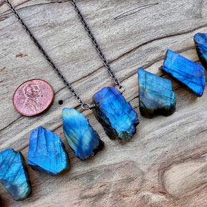 a necklace with blue gemstones, including a large blue crystal, and a copper-colored coin placed on a wooden surface.