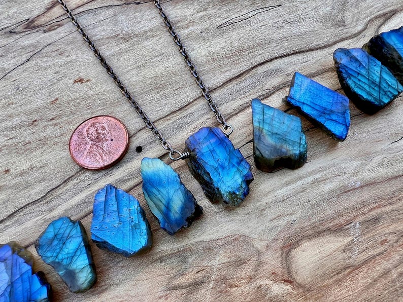 a necklace with blue gemstones, including a large blue crystal, and a copper-colored coin placed on a wooden surface.