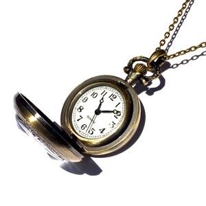 Op de afbeelding: Een gouden zakhorloge met een witte wijzerplaat en zwarte wijzers. Het horloge is open en heeft een ketting eraan.