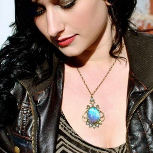 Puede incluir: Una mujer lleva una chaqueta de cuero marr&oacute;n con cremallera y un collar con un colgante de piedra preciosa azul y morado. El collar tiene una cadena dorada y un dise&ntilde;o met&aacute;lico detallado.