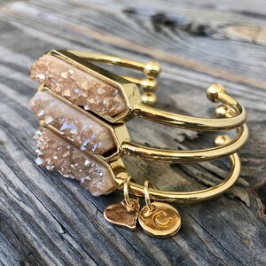 May include: Gold bracelet with three stacked crystal charms and two gold charms, one heart-shaped and one with the letter "C".