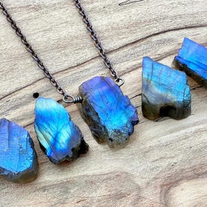 A necklace with a pendant made of blue and green stones, resting on a wooden surface.
