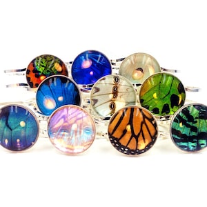 Pode incluir: Um conjunto de dez pulseiras de prata com designs de asas de borboleta coloridas. Cada pulseira apresenta um padrão de asas de borboleta diferente, incluindo azul, verde, laranja e marrom.
