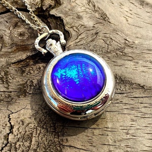 Op de afbeelding: Een zilveren zakhorlogeketting met een blauw en groen iriserend glazen gezicht.