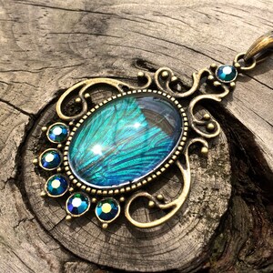May include: A gold-tone pendant necklace featuring a large oval-shaped blue and green iridescent glass cabochon set in a filigree frame. The pendant is surrounded by smaller blue and green rhinestones.