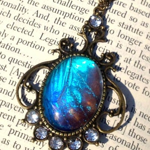 Puede incluir: Un collar con un colgante de bronce con un ala de mariposa azul y marr&oacute;n encapsulada en resina. El colgante est&aacute; rodeado de diamantes de imitaci&oacute;n transparentes.