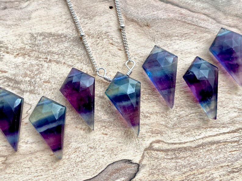 May include: A silver chain necklace with seven iridescent purple, blue, and green fluorite crystal pendants in a diamond shape.