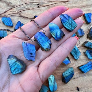 A hand holding a necklace with blue and green stones, as well as some additional blue and green stones scattered on a wooden surface.
