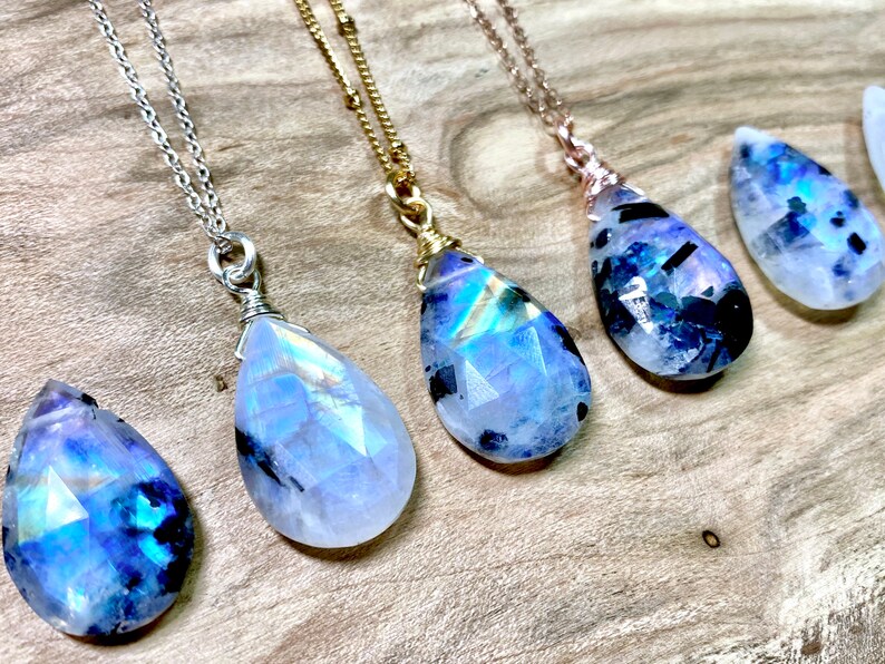 Puede incluir: Cinco collares de plata, oro y oro rosa con colgantes de l&aacute;grima de piedra de luna arco&iacute;ris iridiscente. Los colgantes son facetados y tienen un color azul y blanco.