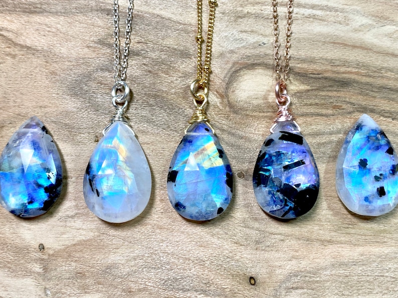 Puede incluir: Cinco colgantes de piedra lunar arco&iacute;ris en forma de l&aacute;grima en cadenas de plata, oro y oro rosa. Los colgantes son facetados y tienen un brillo iridiscente.