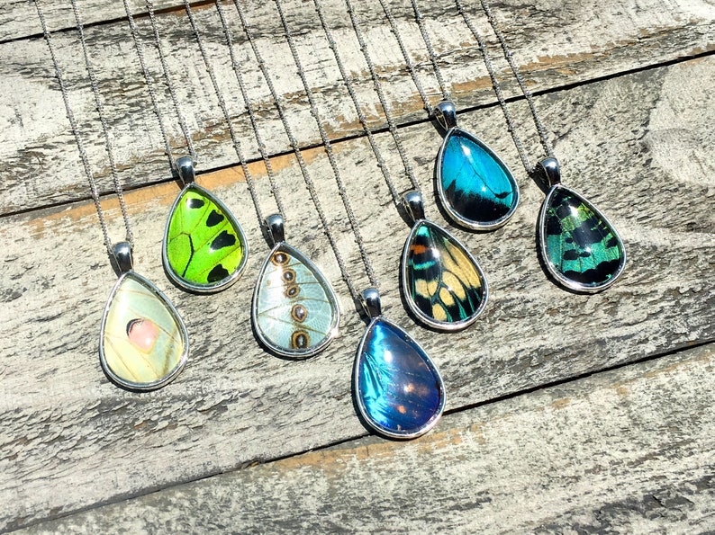 Peut inclure: Un ensemble de huit pendentifs en forme de goutte d'eau pr&eacute;sentant des ailes de papillon conserv&eacute;es. Les pendentifs sont en argent et pr&eacute;sentent une vari&eacute;t&eacute; de couleurs, notamment le vert, le bleu et le jaune.