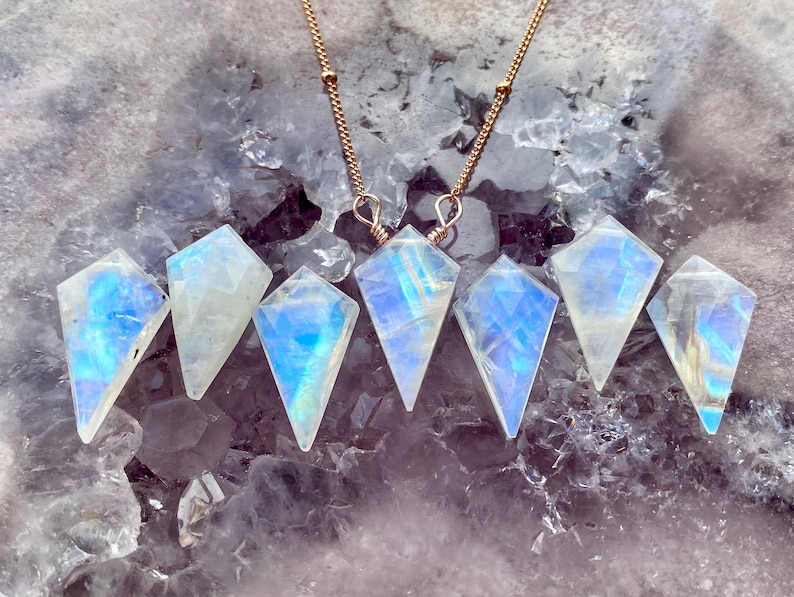 May include: Six iridescent rainbow moonstone pendants on gold chains. The moonstone pendants are faceted and have a teardrop shape.