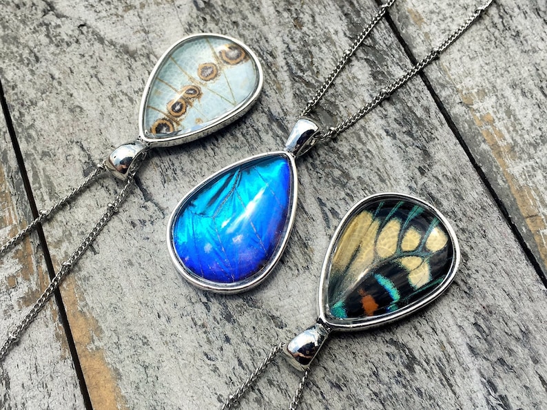Peut inclure: Trois pendentifs en argent en forme de goutte d'eau avec des ailes de papillon ench&acirc;ss&eacute;es dans de la r&eacute;sine transparente. Les pendentifs sont sur des cha&icirc;nes en argent.