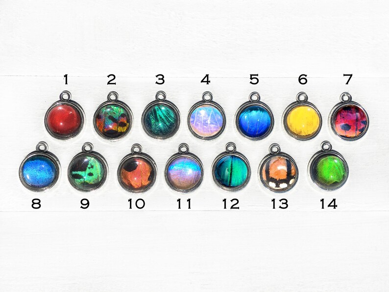 May include: Assortment of 14 round pendants featuring colourful butterfly wings encased in silver settings. The pendants are numbered 1 through 14.