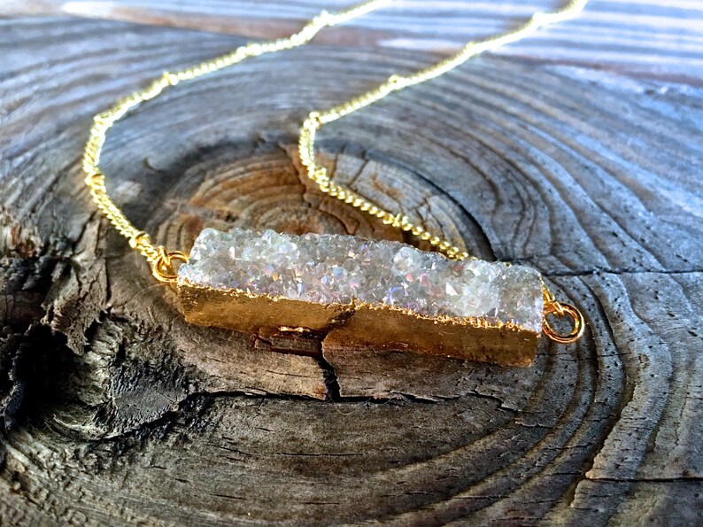May include: A gold chain necklace with a white crystal bar pendant. The crystal bar is encased in gold metal and has a rough, natural texture.