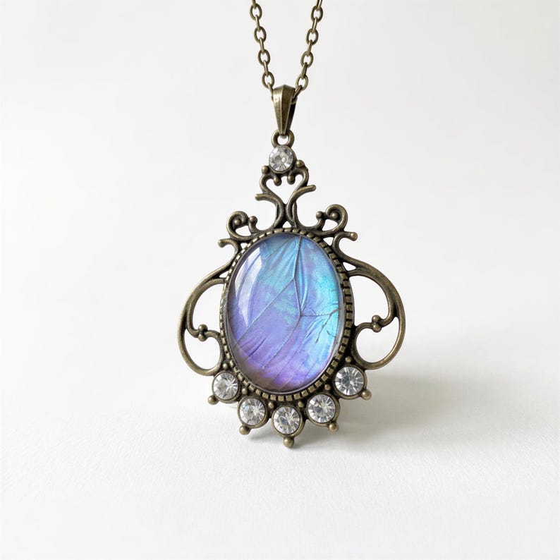 A necklace with a pendant featuring a blue butterfly wing encircled by an ornate, decorative metal frame.