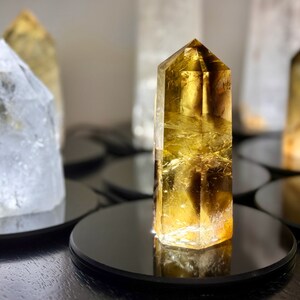 May include: A collection of clear and yellow crystal points on black circular bases. The crystals are arranged in a row, with the yellow crystal point in the center.