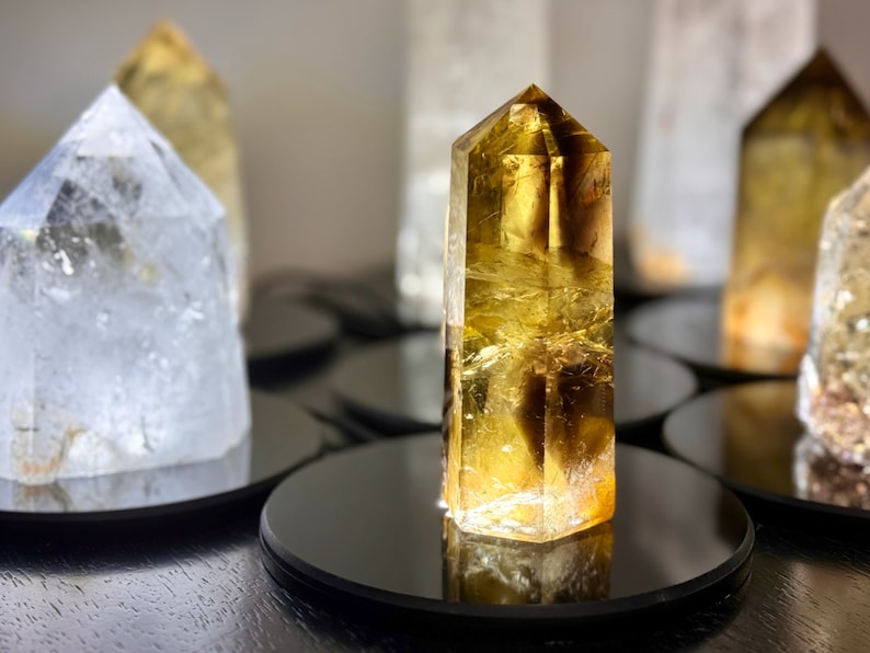 May include: A collection of clear and yellow crystal points on black circular bases. The crystals are arranged in a row, with the yellow crystal point in the center.
