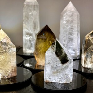 May include: A collection of seven clear quartz crystal points, some with a smoky or golden hue, displayed on black circular bases.