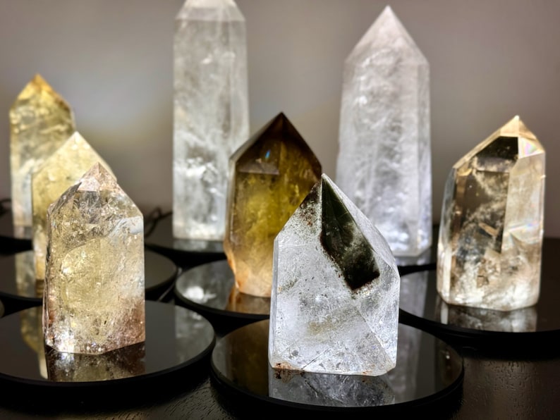 May include: A collection of seven clear quartz crystal points, some with a smoky or golden hue, displayed on black circular bases.