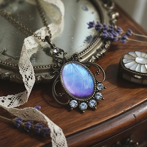A vintage-style necklace with a blue and purple stone pendant, adorned with small blue gemstones, rests on a wooden surface. The necklace is complemented by a lace doily and a small white box, creating an elegant and nostalgic display.