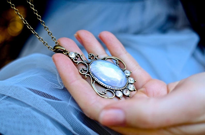 A hand holding a decorative pendant necklace with a blue stone.
