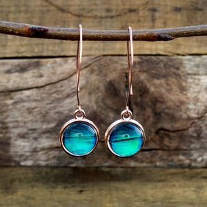 May include: A pair of rose gold dangle earrings with round blue and green iridescent glass stones.