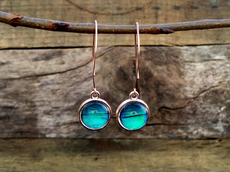 May include: A pair of rose gold dangle earrings with round blue and green iridescent glass stones.