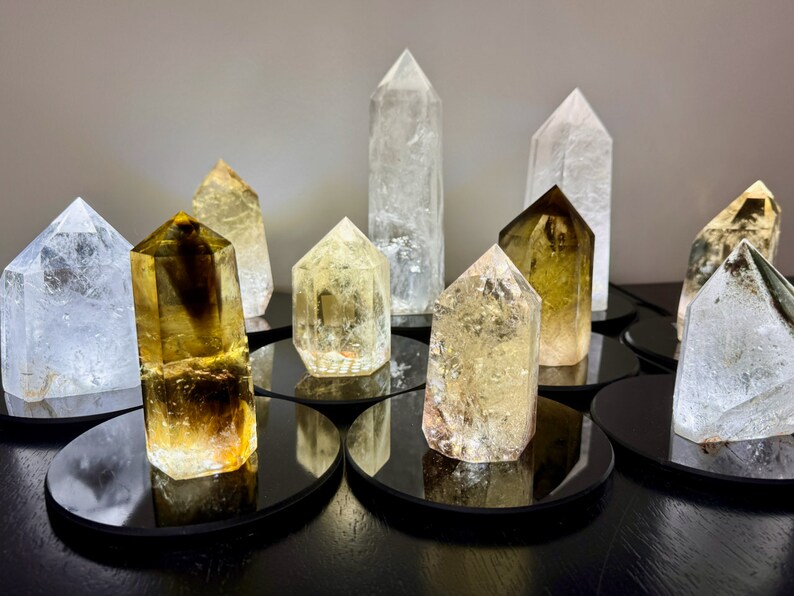 May include: A collection of clear and yellow crystal points on black circular bases. The crystals are arranged in a semi-circle on a dark surface.