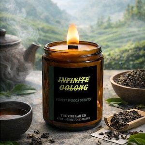 Könnte beinhalten: Eine brennende Infinite Oolong Kerze in einem braunen Glas mit einem schwarzen Etikett. Auf dem Etikett steht "Infinite Oolong Forest Woods Scents" und "The Vibe Lab Co". Die Kerze ist von Teeblättern, einer Teekanne und einer Schüssel umgeben.