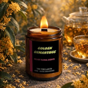Könnte beinhalten: Eine brennende Kerze in einem braunen Glas mit einem schwarzen Etikett. Auf dem Etikett steht "Golden Osmanthus, Velvet Floral Scents". Die Kerze hat einen Holzdocht und ist von gelben Blüten und Tee umgeben. Der Text "The Vibe Lab Co, ASMR - Ignite Your Senses" ist ebenfalls sichtbar.