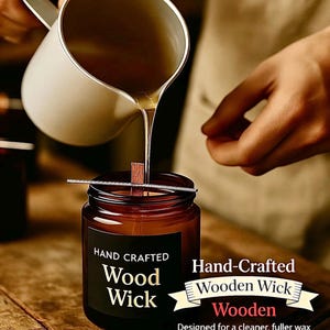 May include: A candle-making process is shown, with a brown glass jar candle featuring a wooden wick. The jar has a black label with the words "Hand Crafted Wood Wick." A person is pouring liquid wax into the jar from a white pitcher.