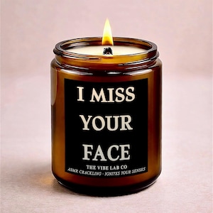 May include: A lit brown glass candle jar with a black label that reads "I MISS YOUR FACE." The candle is from The Vibe Lab Co. and is advertised as ASMR crackling that ignites your senses. The candle has a lit wick.
