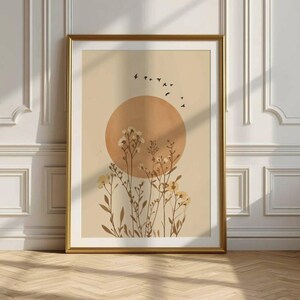 Puede incluir: Una impresión artística enmarcada con un diseño minimalista. La obra de arte representa un gran círculo naranja que representa el sol, con siluetas de pájaros volando por encima. Delicados elementos florales están dispuestos debajo del sol, sobre un fondo neutro.