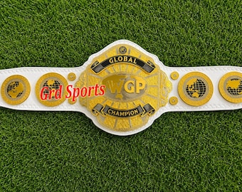 May include: A white championship belt featuring a large central gold plate with the text Global WGP Champion. The belt includes four smaller circular gold plates depicting world maps and the red text Grd Sports printed on the left side.