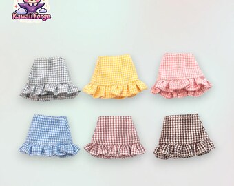 May include: Six miniature plaid skirts with ruffled hems in various colors: gray, yellow, pink, blue, brown, and black.