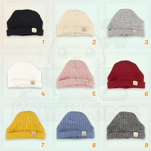 Può includere: Nove berretti lavorati a maglia in vari colori: nero, crema, grigio, bianco, rosa, rosso, giallo, blu e antracite. Ogni berretto ha una piccola etichetta quadrata. I berretti sono disposti a griglia.