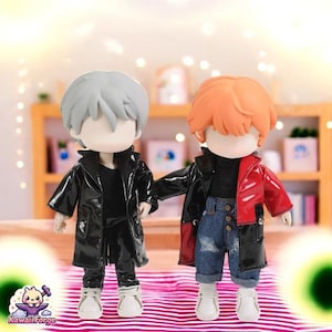 May include: Two small dolls wearing black and red leather jackets. The doll on the left has silver hair and is wearing black pants. The doll on the right has orange hair and is wearing blue jeans.