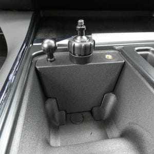 May include: A black car interior with a center console. A black ball mount and a black device mount are installed in the console. The console has a textured surface and a small storage area.
