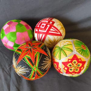 Puede incluir: Cuatro bolas Temari coloridas con intrincados patrones geométricos y florales. Las bolas presentan una variedad de colores, incluyendo verde, rosa, rojo, amarillo y negro. Cada bola muestra un detallado trabajo de bordado.