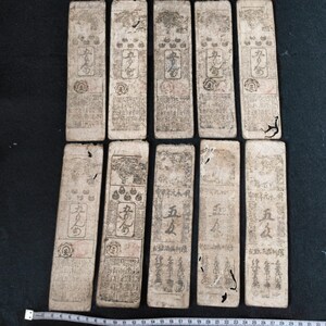 May include: A collection of ten rectangular, aged paper artifacts with intricate black calligraphy and illustrations. The paper has a worn, off-white color, with visible signs of age and use. The artifacts appear to be historical documents or prints, possibly from East Asia.